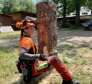 Frau in Warnfarben kniet neben Baumstamm