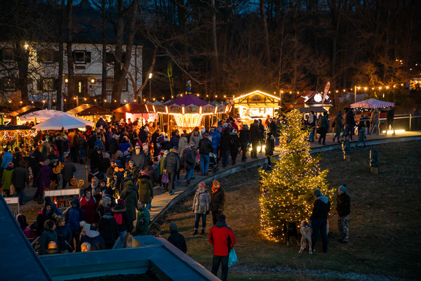 Ein erleuchteter Weihnachtsbaum, Marktstände und viele Besucher in den Abendstunden