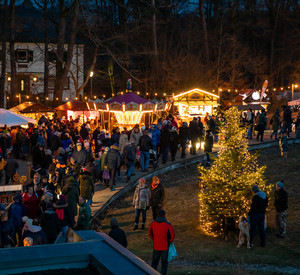 Ein erleuchteter Weihnachtsbaum, Marktstände und viele Besucher in den Abendstunden
