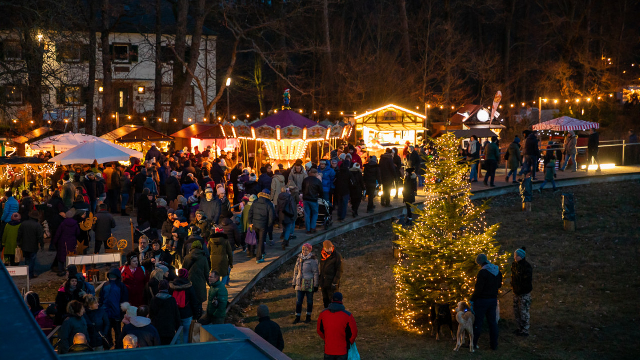 Ein erleuchteter Weihnachtsbaum, Marktstände und viele Besucher in den Abendstunden