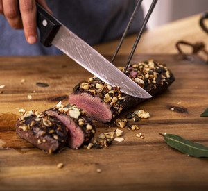 Das Bild zeigt eine Person, die einen fertig zubereiteten Rehrücken auf einem Holzbrett in kleine Portionen schneidet
