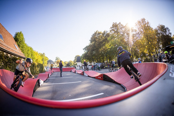 zwei Menschen auf Fahrrädern fahren über einen roten geschwungenen Parcours