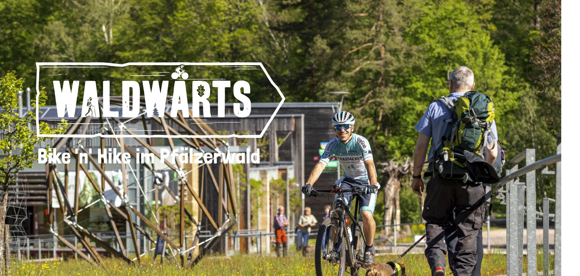 Das Bild zeigt einen Mountainbiker und Wanderer vor dem Haus der Nachhaltigkeit