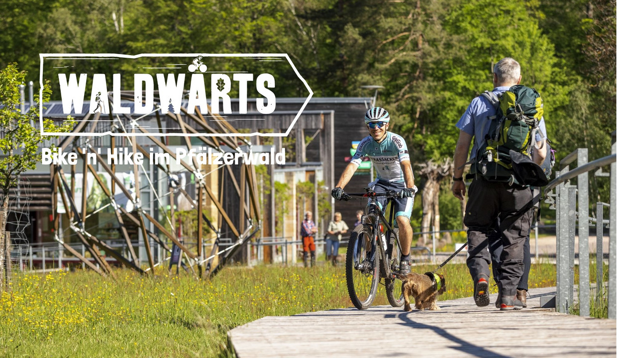 Das Bild zeigt einen Mountainbiker und Wanderer vor dem Haus der Nachhaltigkeit