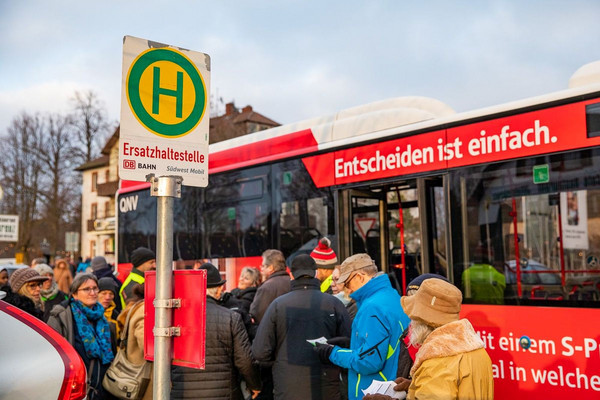 Ein Linienbus steht hinter einem Schild mit der Aufschrift "Ersatzhaltestelle", drumherum sind einige Menschen in Winterkleidung zu sehen.