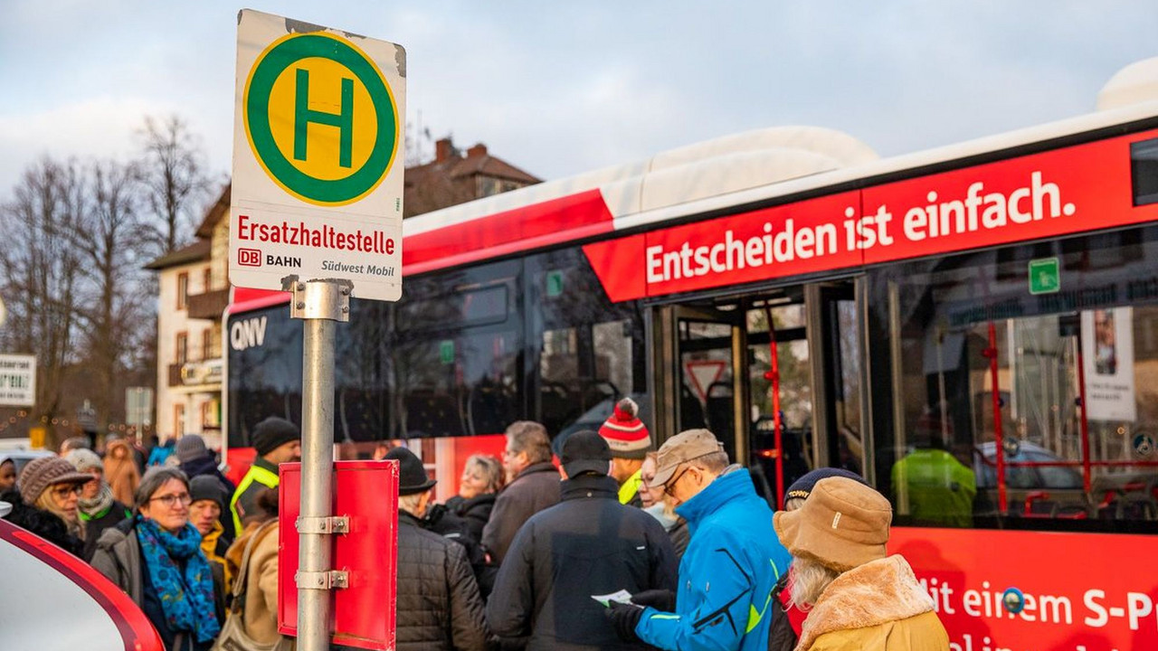 Ein Linienbus steht hinter einem Schild mit der Aufschrift "Ersatzhaltestelle", drumherum sind einige Menschen in Winterkleidung zu sehen.