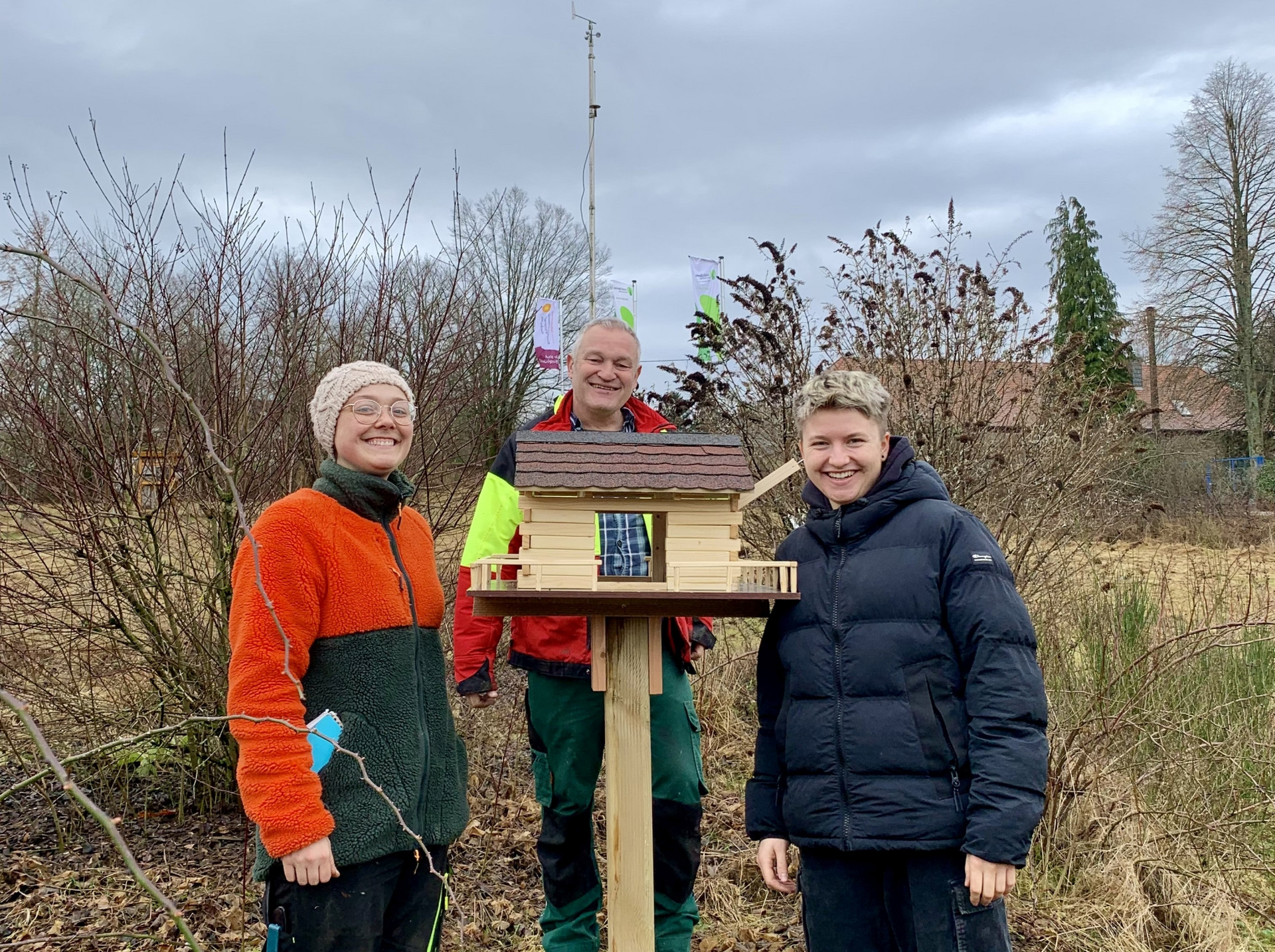 Zwei Frauen und ein Mann stehen um ein neues Vogelhaus herum