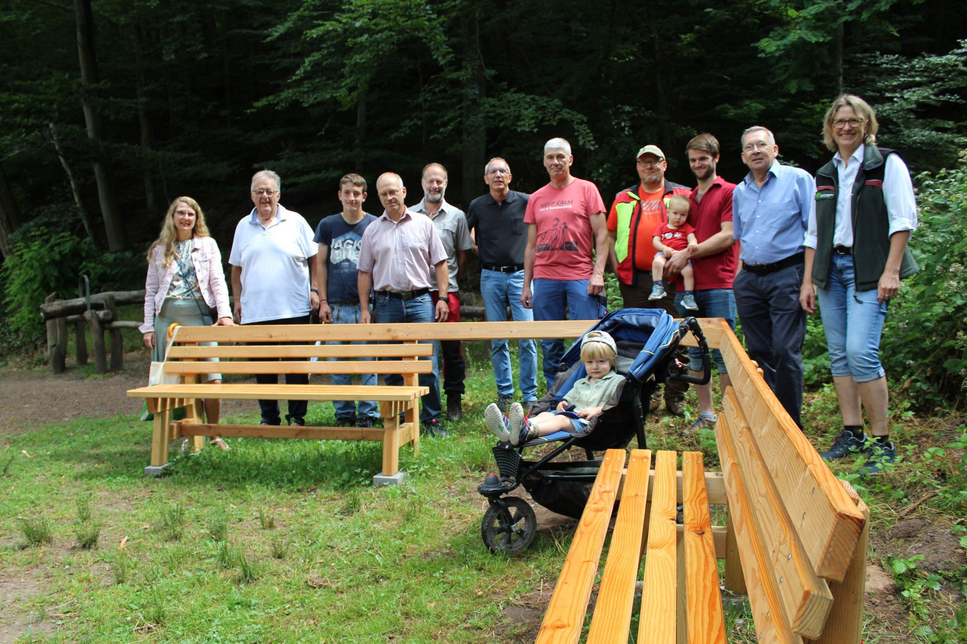 Begegnungsbank am Eiswoog Begegnungsbank steht auf einer schattigen Wiese, viele Leute stehen dahinter.